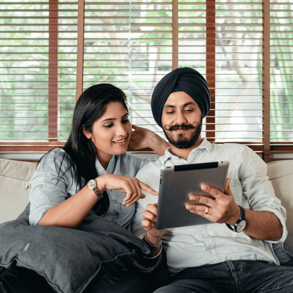 man and woman sit on a couch looking at an ipad