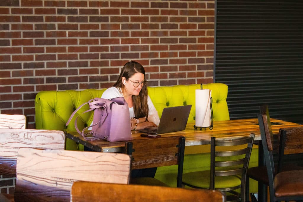 Lindsey Miller leading a meeting. On a computer at a restaurant, sitting on a lime green chair and looking at a computer