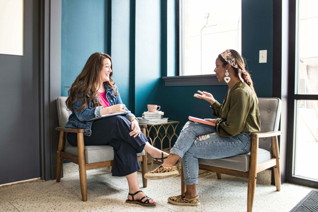 A woman telling a story to another woman while they sit in a lobby.