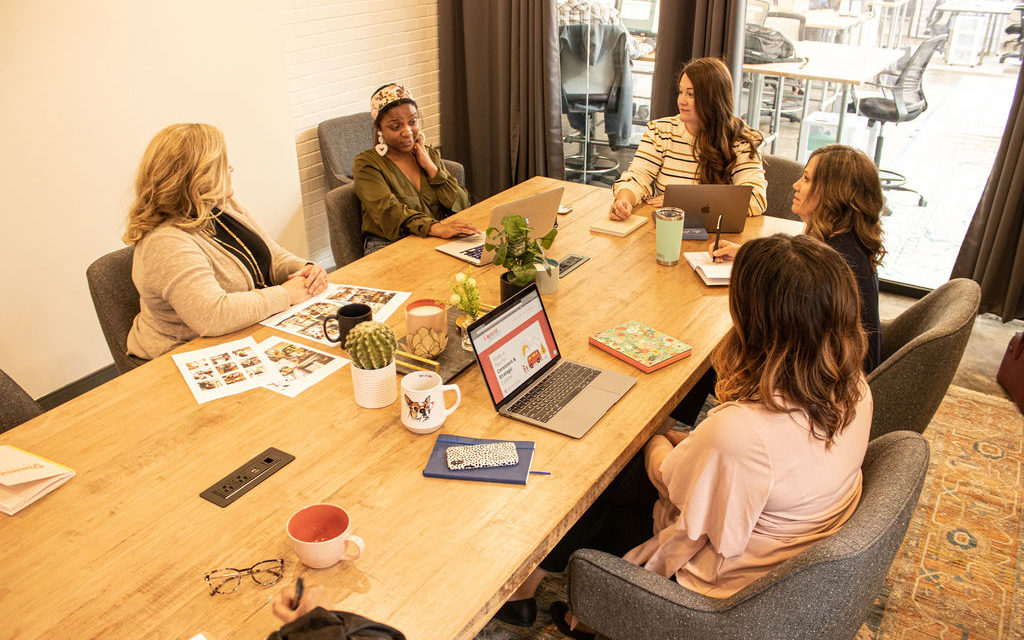 A group of women, sitting around a conference room table, discussing the differences in content writing vs. copywriting.
