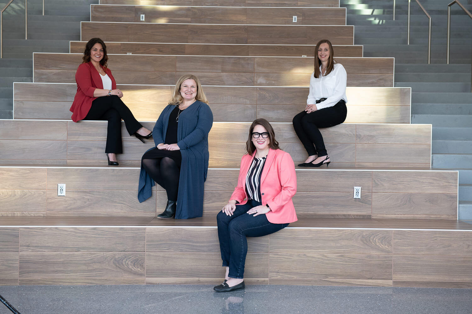 Four women sit staggered on stairs smiling at the camera