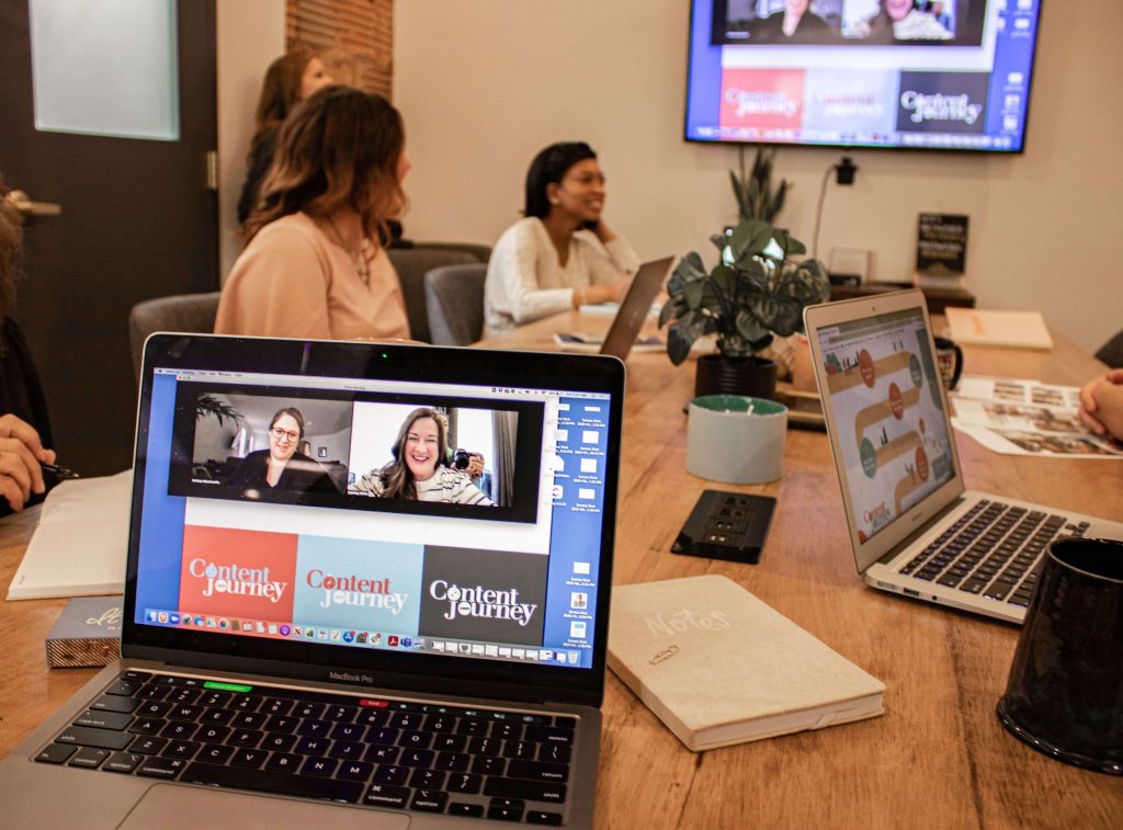 A laptop screen showing a webinar while people sit around a conference room table