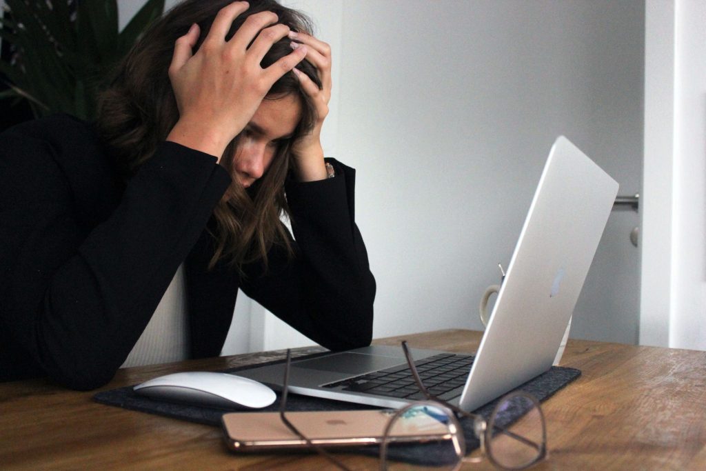 A woman sitting in front of a laptop with her head in her hands.