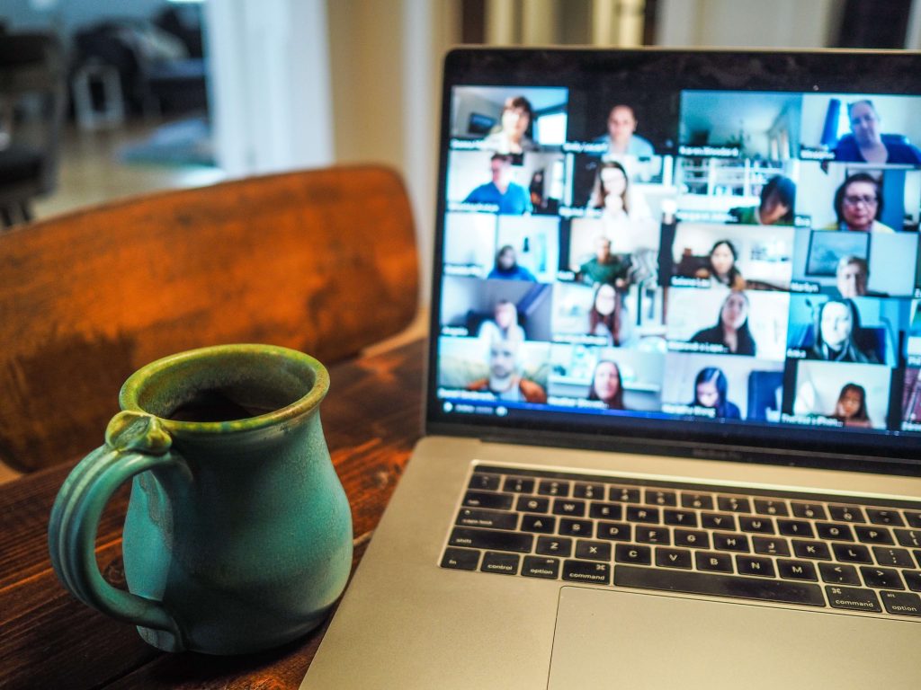 A laptop screen displaying a Zoom meeting or webinar with a coffee mug sitting next to the computer.